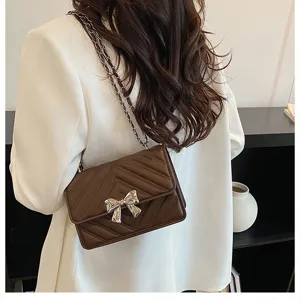 Detail shot of brown quilted leather shoulder bag with chic silver bow and chain strap.
