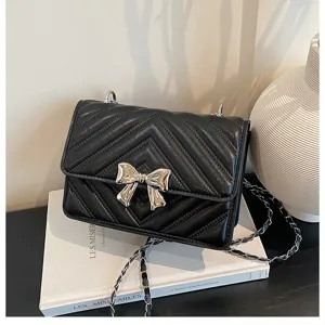 Detail view of black quilted leather crossbody bag with silver bow and chain strap.