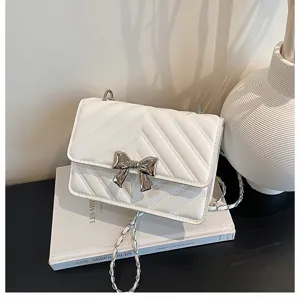 White quilted chain shoulder bag with silver bow accent, stylish detail photography.