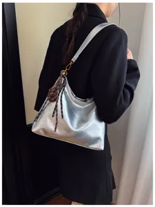 Detail view of a chic silver shoulder bag worn by a model, featuring trendy decorative straps.