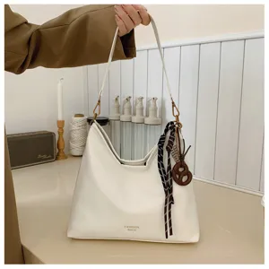 White leather hobo shoulder bag detail shot showing elegant strap hardware and chic ribbon charm.