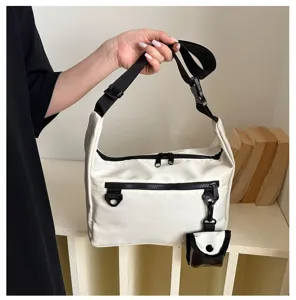 Close-up detail of the casual white crossbody messenger bag with black strap and hanging pouch.