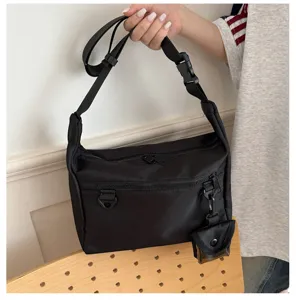 Detailed view of black nylon messenger bag with zipper pockets and small charm, practical design.