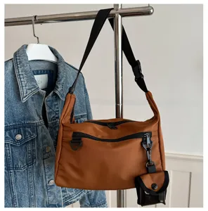 Minimalist brown messenger bag with front zipper pocket, black strap and small detachable pouch.