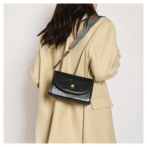 Detail view of black small square crossbody bag with ethnic wide strap and gold flower decor.