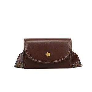 Brown leather crossbody bag with ethnic strap and metal flower detail, stylish and compact.