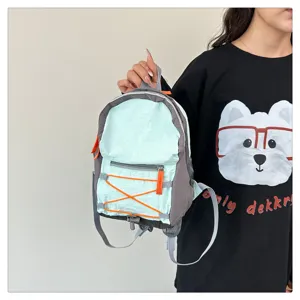 Close-up detail shot of a stylish light blue and gray mini backpack with orange elastic cords.