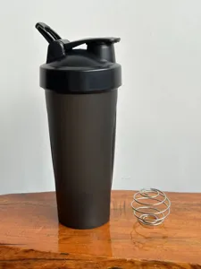 Detailed view of black fitness protein shaker bottle with metal whisk ball on wooden table.