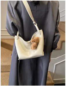 Détail du sac porté épaule minimaliste en cuir blanc avec charmant pendentif d'ours en peluche.