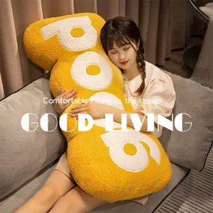 Close-up view of the cozy yellow letter plush pillow in a warm living room lifestyle setting.