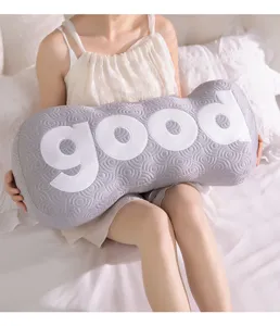 Close-up detail of a long gray plush bolster pillow featuring large white good letters.