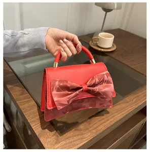 Detail view of red women handbag with elegant bow decoration and curved bottom design.