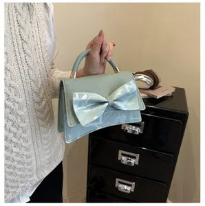 Close-up detail of the elegant sage green handbag featuring a chic front bow and structured top handle.