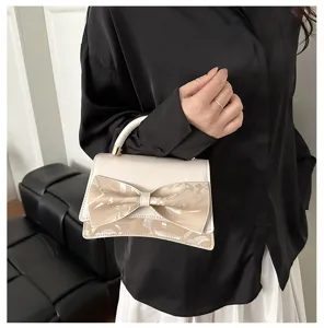 Detail shot of elegant beige women handbag featuring a glossy bow and top handle.