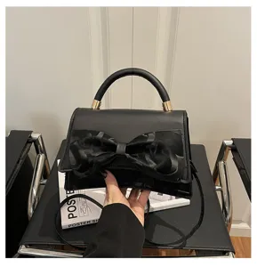 Black minimalist handbag detail featuring an elegant bow decoration and sturdy top handle.