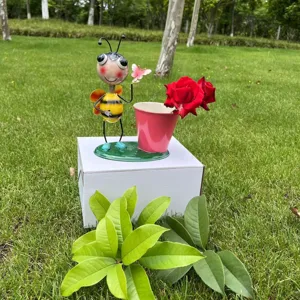 Vista ravvicinata del simpatico vaso di fiori ape in metallo su una scatola bianca all'aperto.