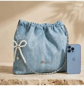Λεπτομερής εικόνα της κομψής τσάντας denim με φιόγκο πέρλας και μεταλλική αλυσίδα.