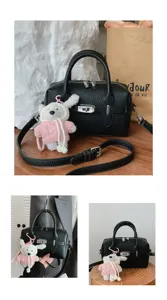 Bolso de mano de piel granulada negra con colgante de oso y cierre giratorio.