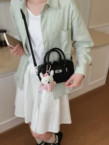 Bolso de mano elegante de cuero negro con textura y llavero de conejo adorable y candado.