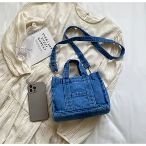 Sac bandoulière en denim décontracté avec poignées et sangle réglable, présenté sur robe blanche.