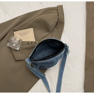 Vue détaillée du sac bandoulière en jean décontracté, disposé avec style sur un lit.