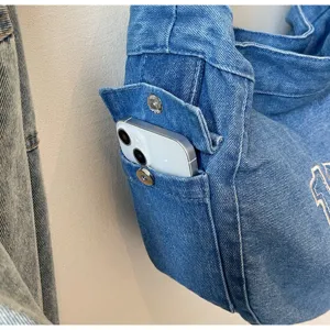 Vintage denim shoulder bag detail showing spacious front pocket with phone storage capacity.