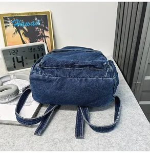 Denim backpack detail featuring dark blue fabric texture, front zipper pocket and adjustable straps.