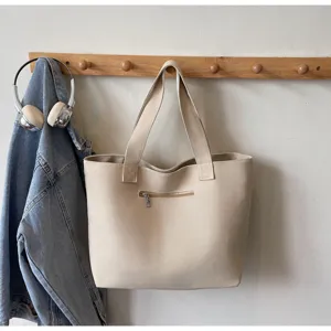 Detail view of beige canvas tote bag hanging on wooden wall hook with casual lifestyle style.