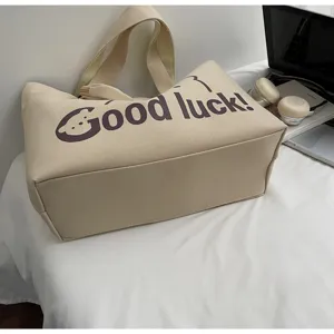 Close-up of stylish beige canvas tote bag with Good luck text design for daily commute.