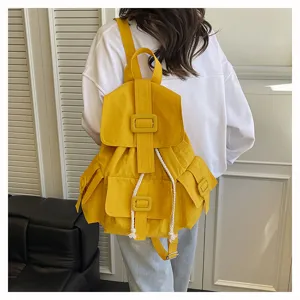 Detalle de mochila de lona amarilla con solapa, cierre de hebilla y correas estilo casual.