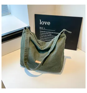 Detalle del bolso de hombro de lona verde con correa ancha y diseño minimalista.