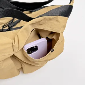 Detailed view of khaki canvas crossbody bag featuring black strap and functional front pocket.
