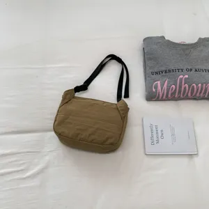 Detail view of the brown nylon crossbody bag with black straps in a casual everyday scene setup.