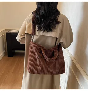 Detail view of the brown corduroy shoulder bag worn by a model in a cozy indoor setting.