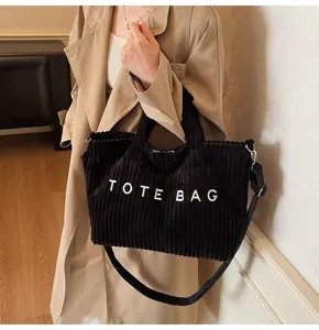 Close-up shot of black corduroy tote bag showing textured fabric and shoulder strap detail.