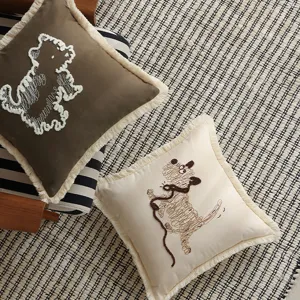 Close-up of decorative pillow cover with cute embroidered dog design and stylish fringe trim.