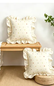 Cuscino decorativo in stile crema con bordo arricciato e grazioso motivo floreale ricamato.