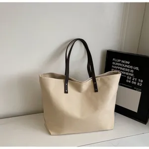 Canvas tote bag detail view, beige fabric with dark brown shoulder straps and metal rivets.