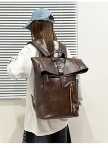 Detail shot showing the dark brown leather roll-top backpack worn by a model from the back.