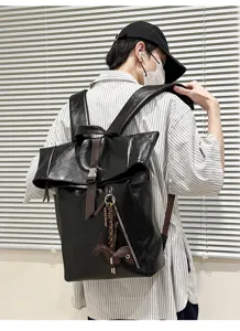 Detailed shot of black leather rolltop backpack showcasing metal buckle and charm.