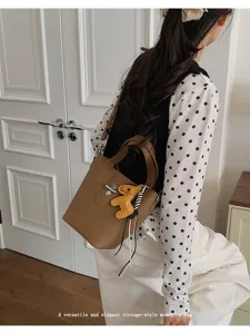Casual bruine lederen emmertas handtas met handvatten en schattige hanger voor dagelijks gebruik.
