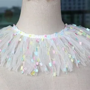 Close-up detail of white mesh tulle trim with colorful confetti tassels for garment decoration.