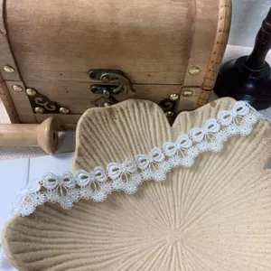 Detailed close-up of white bow lace trim, delicate embroidery texture for DIY garments & crafts.
