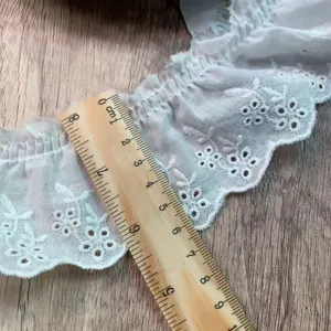 White hollow embroidered ruffled lace trim detail shot showing width with wooden ruler.