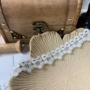 Exquisite 3cm white bow lace trim detail close-up, hollow embroidery fabric for DIY crafts.