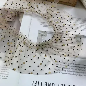 Close-up detail of beige mesh lace trim with black polka dots and gold foil ruffles.