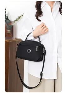Detailed shot of a black nylon crossbody bag worn by a model, showing the front pocket design.