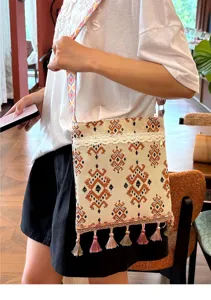 Primer plano del bolso bandolera tejido estilo boho con bordado étnico, encaje y borlas finas.