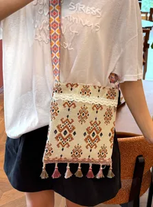 Detalle de bolso bandolera tejido estilo étnico con correas de colores y borlas finas.