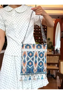 Vista detallada del bolso cruzado de estilo étnico con patrones geométricos y borlas.